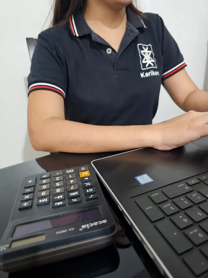 Kariken staff in a company shirt at a desk with a calculator and laptop