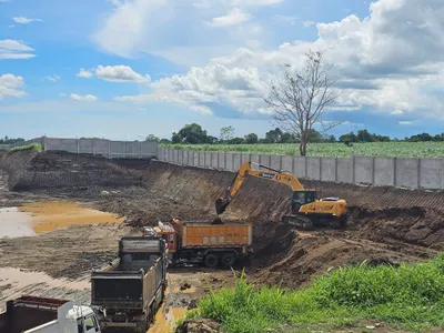 Excavator and dump trucks working along a new concrete perimeter fence